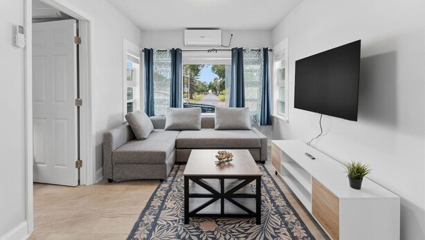 Una sala de estar moderna con un sofá, una mesa de centro, televisor y vistas a través de amplios ventanales.