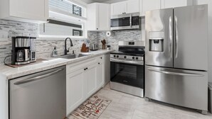 Cocina moderna con armarios blancos, electrodomésticos de acero inoxidable, cafetera y horno empotrado.