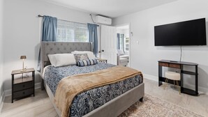 Un dormitorio con cama, mesitas de noche, un escritorio, una silla, un televisor y una ventana con cortinas.
