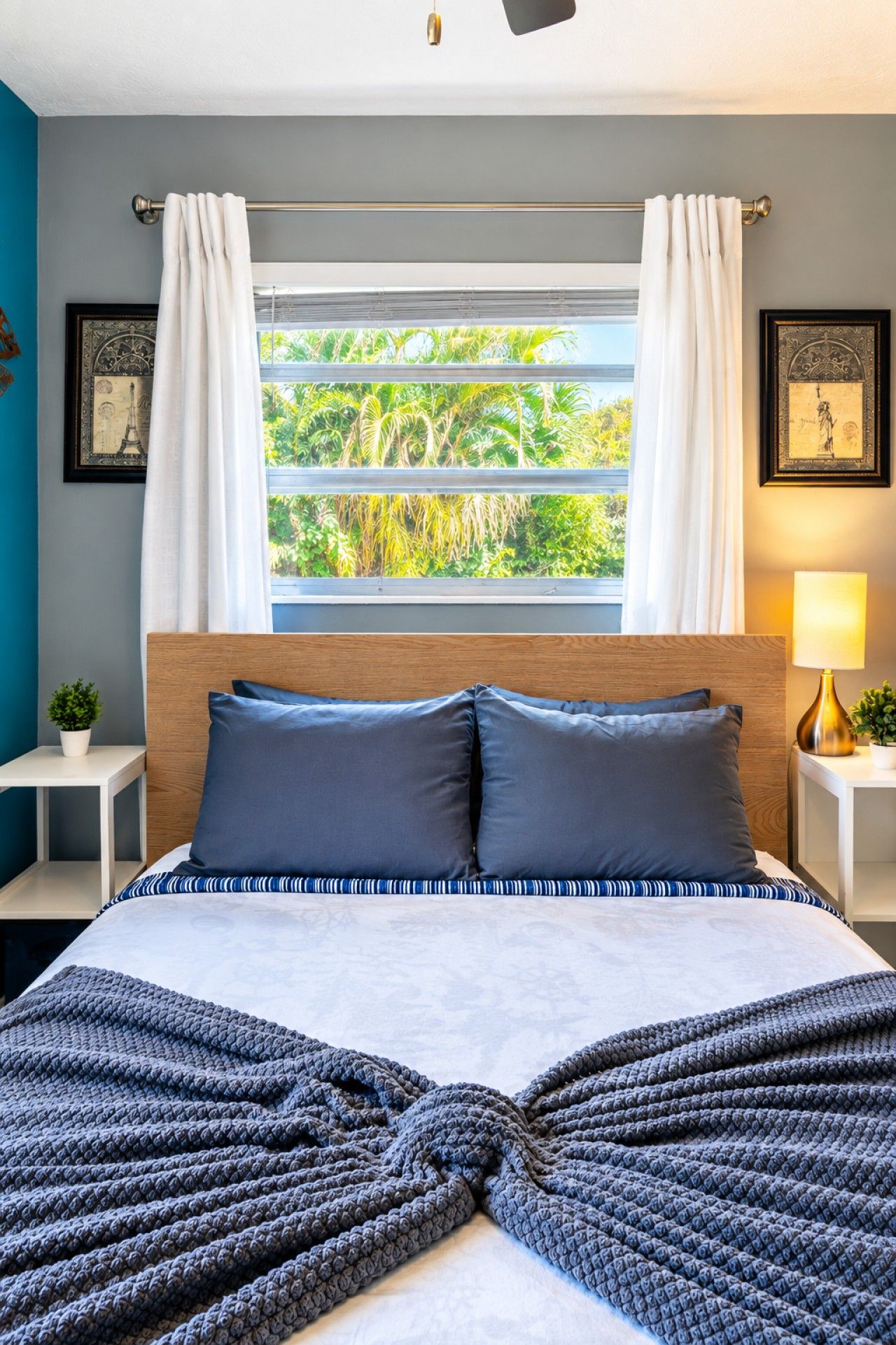 A bedroom with a bed, a window with curtains, a bedside lamp, and a framed picture on the wall.