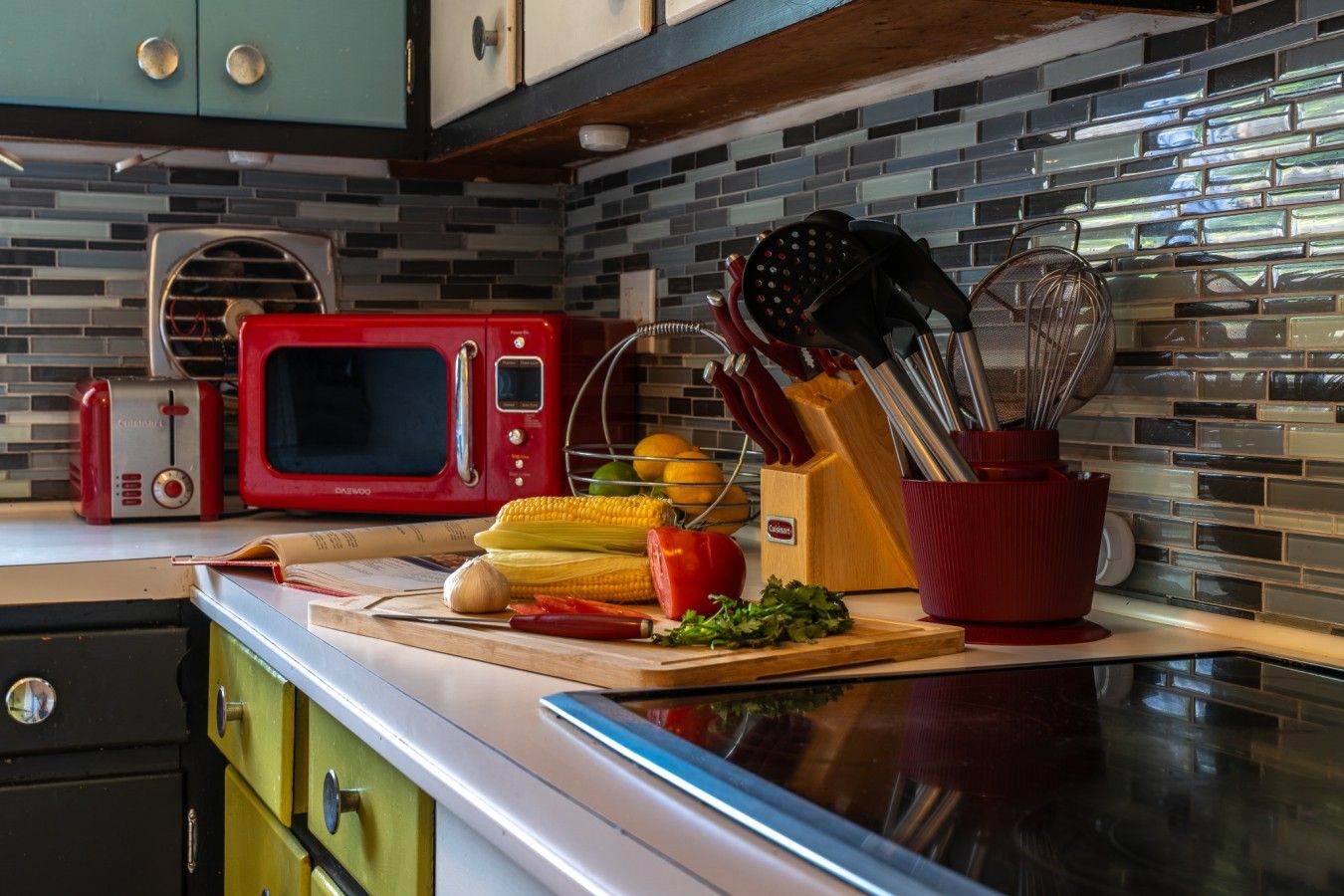 A kitchen with a red microwave, a cutting board with vegetables, and a knife block.