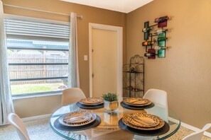 A dining area with a glass table, four chairs, and a decorative metal rack with bottles. - Coastal Retro Haven: Private Yard • Near Beach (Sarasota)