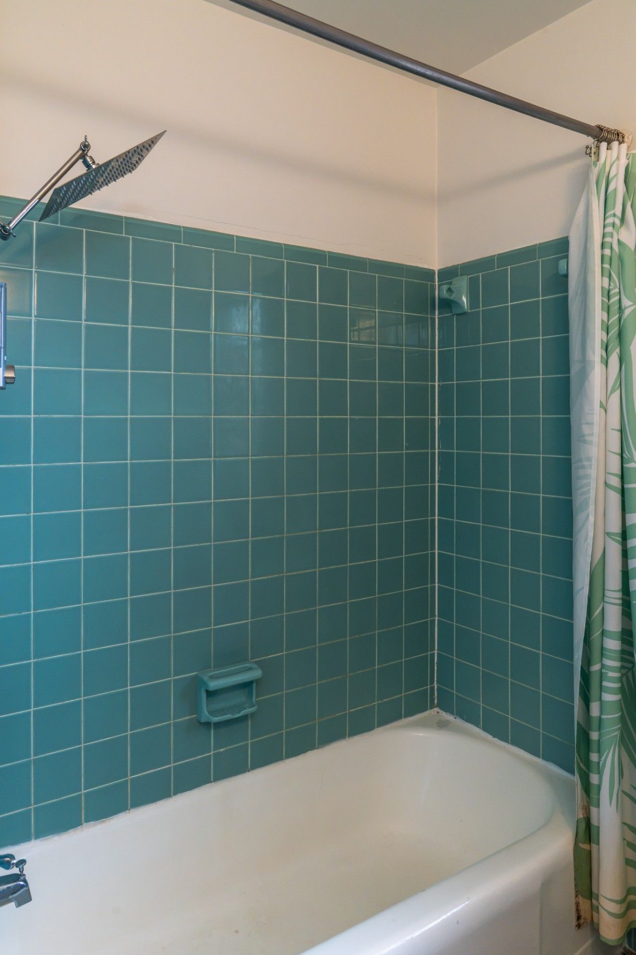 Ein Badezimmer mit türkis-gefliesten Wänden, einer weißen Badewanne und einer Duschvorhang.