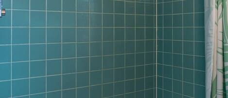 Ein Badezimmer mit türkis-gefliesten Wänden, einer weißen Badewanne und einer Duschvorhang.