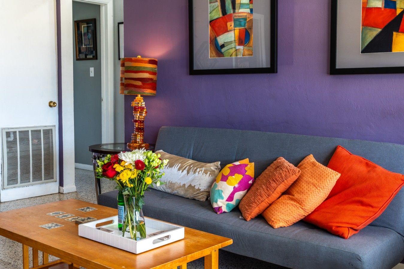 Un salon avec un canapé, des coussins colorés, un vase de fleurs et une œuvre d’art abstrait accrochée au mur.