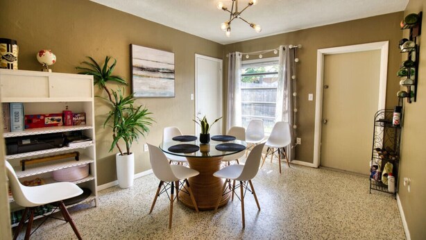 A dining area with a round table, chairs, a potted plant, and a bookshelf. - Coastal Retro Haven: Private Yard • Near Beach (Sarasota)