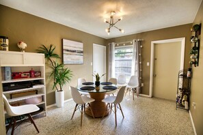 A dining area with a round table, chairs, a potted plant, and a bookshelf. - Retro Sarasota Haven: Private Yard| BBQ |Downtown (Sarasota)