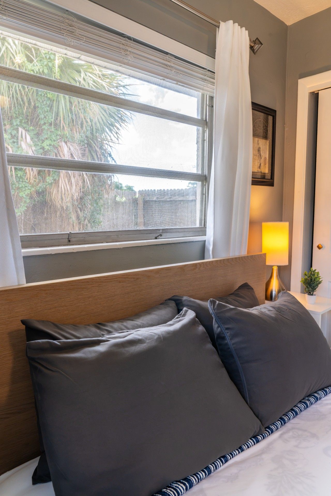 Quarto de hotel com cama, mesa de cabeceira, abajur e janela com cortinas.
