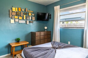 A bedroom with a bed, a dresser, a TV mounted on the wall, and a window with curtains. - Coastal Retro Haven: Private Yard • Near Beach (Sarasota)