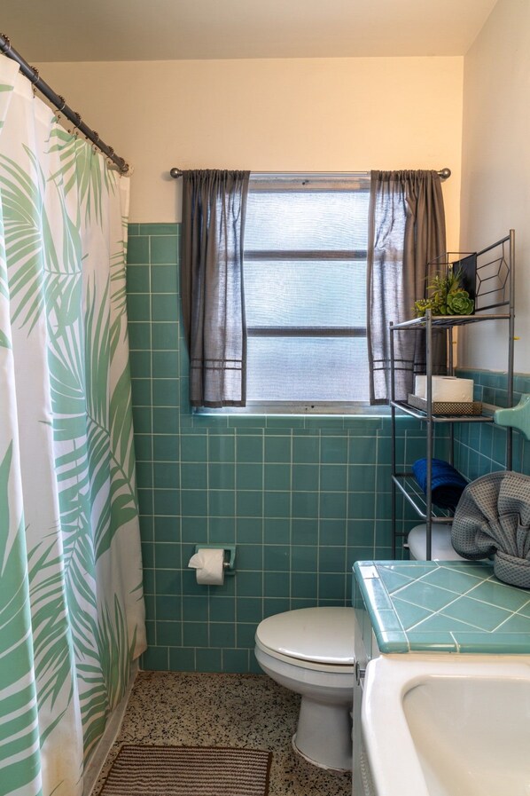A bathroom with a toilet, a sink, a shower curtain, a window, and a towel rack. - Coastal Retro Haven: Private Yard • Near Beach (Sarasota)