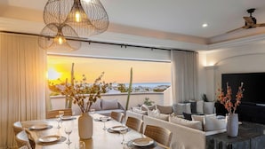 Ein Essbereich mit Sonnenuntergangblick, ein Wohnzimmer mit Fernseher und ein Balkon mit Aussicht.