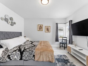 A bedroom with a bed, a TV, a chair, and artwork on the wall. - Clearwater Charm Unit D (Clearwater)