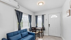 Olohuoneessa on sininen sohva, ruokapöytä tuoleineen, pyöreä puinen sivupöytä ja valkoinen ovi.
