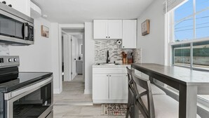 A modern kitchen with white cabinetry, a built-in microwave, and a dining area with a wooden table and chairs. - Clearwater charm 1/1-A (Clearwater)
