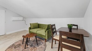 Una habitació amb un sofà verd, una taula de fusta, una cadira, una catifa petita i una làmpada al sostre.