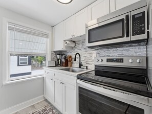 A kitchen with white cabinets, a stainless steel microwave, a built-in oven, and a window with blinds. - Clearwater charm top unit B (Clearwater)