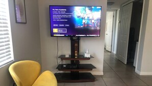 Een woonkamer met een aan de muur bevestigde televisie, een gele stoel en een houten tv-meubel.