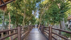 A wooden boardwalk with metal railings, surrounded by trees and vegetation. - Casa Amaya - A comfortable place to enjoy the Riviera Maya with your family. (Puerto Morelos)