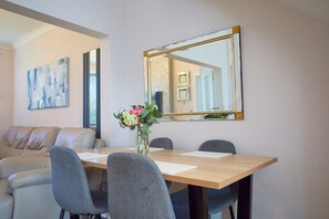 A dining area with a wooden table, four grey chairs, a vase with flowers, and a large mirror on the wall.