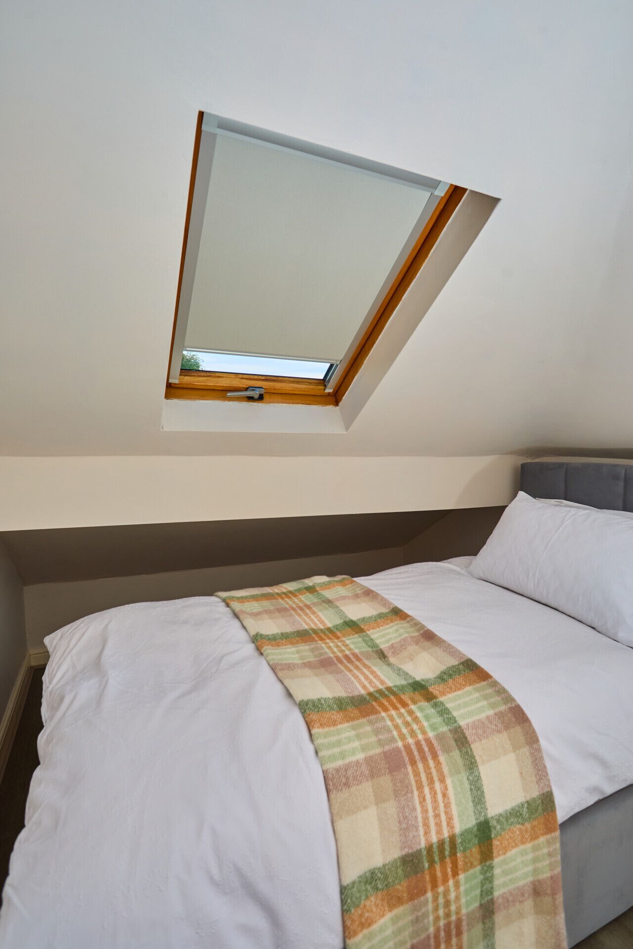 A bedroom with a skylight, a bed with white bedding, and a plaid blanket.