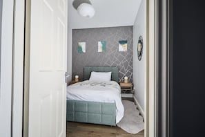 A bedroom with a bed, a nightstand, a wall-mounted mirror, and a geometric-patterned wall.