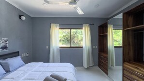 Een slaapkamer met een bed, een plafondventilator, een raam met gordijnen en een kledingkast.