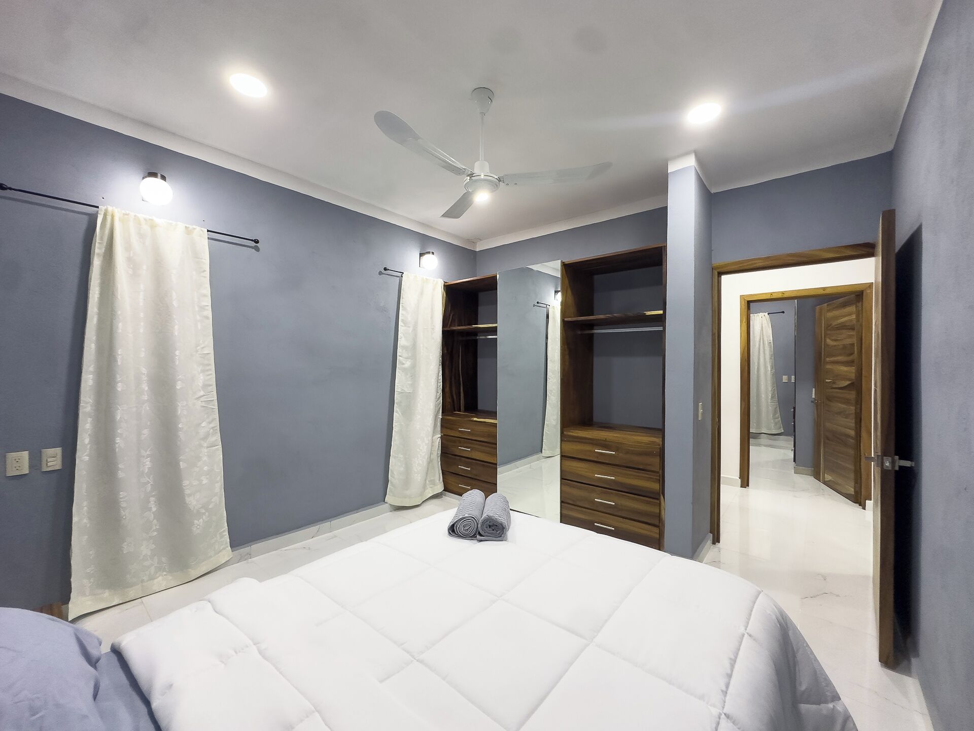 Un dormitorio con cama, ventilador de techo, armario y espejo.