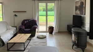 Uma sala de estar com sofá, mesa de centro, televisão, lareira e vista para um jardim verdejante através de uma porta de vidro.
