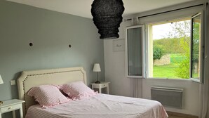 Quarto com cama, mesas de cabeceira, janela e vista para o verde.