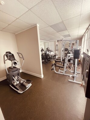 Ein Fitnessraum mit Laufbändern, Kraftgeräten und einem an der Wand befestigten Ergometer.