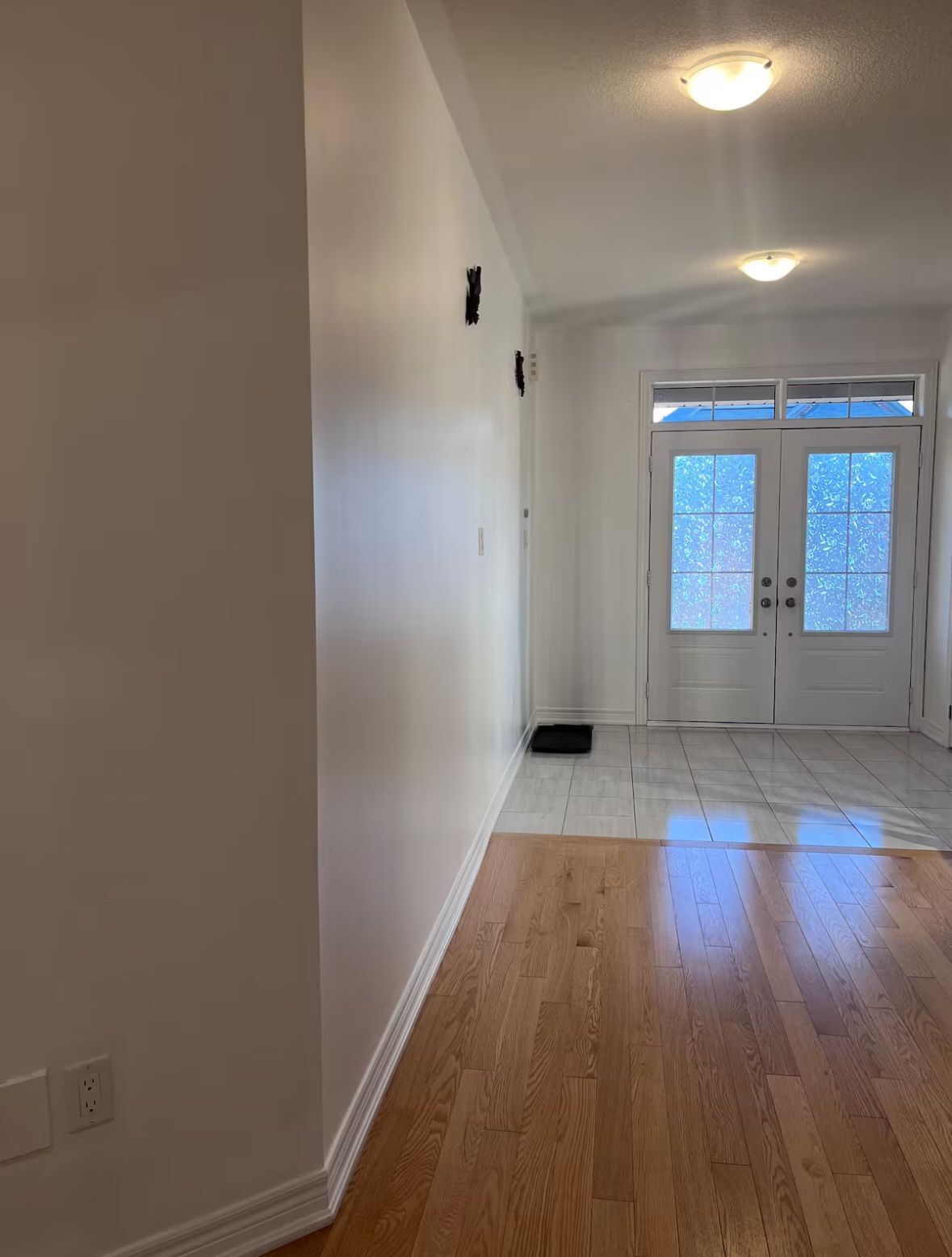 Una habitación con suelo de madera, paredes blancas, una puerta con paneles de vidrio esmerilado y una lámpara en el techo.