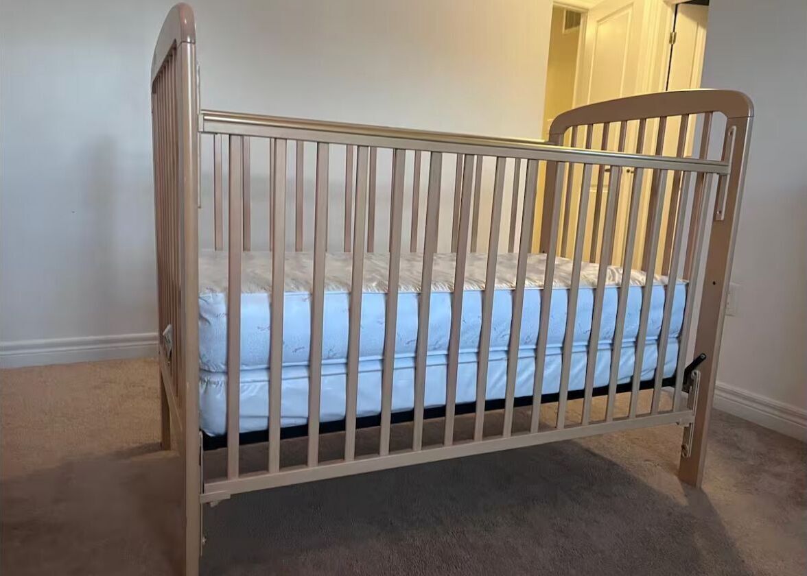 A crib with a mattress, a wooden headboard, and a metal rail.