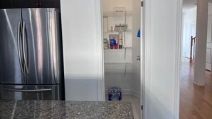 Een keuken met een roestvrijstalen koelkast, een granieten aanrechtblad en een witte deur naar een kast met planken en een verbanddoos.