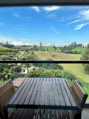 Una mesa y banco de madera en un balcón con vistas a un paisaje verde y casas.