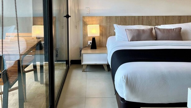 A modern hotel room with a large bed, a bedside table with a lamp, a glass partition, and a view of the outside. - Fully Equipped Suite Near JMC Airport (Rionegro)