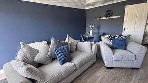 A living room with a grey sofa, a blue armchair, and a small table with a vase.