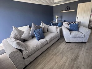 Een woonkamer met een grijze bank, een blauwe fauteuil en een kleine tafel met een vaas.