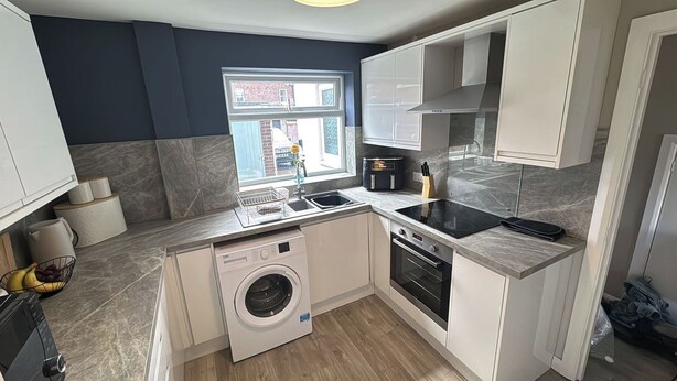 A compact kitchen with a washing machine, oven, and a window with a view of the street.