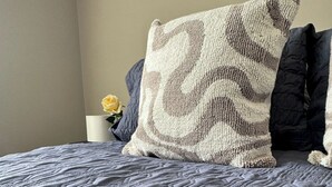 A bed with a textured grey quilt and a patterned pillow.