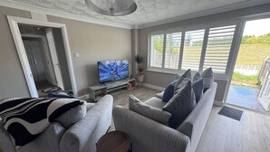 A modern living room with a grey sofa set, a television, and a view of the outdoors.