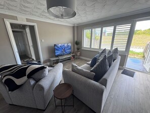 Een moderne woonkamer met een grijze zithoek, een televisie en uitzicht op het groen.