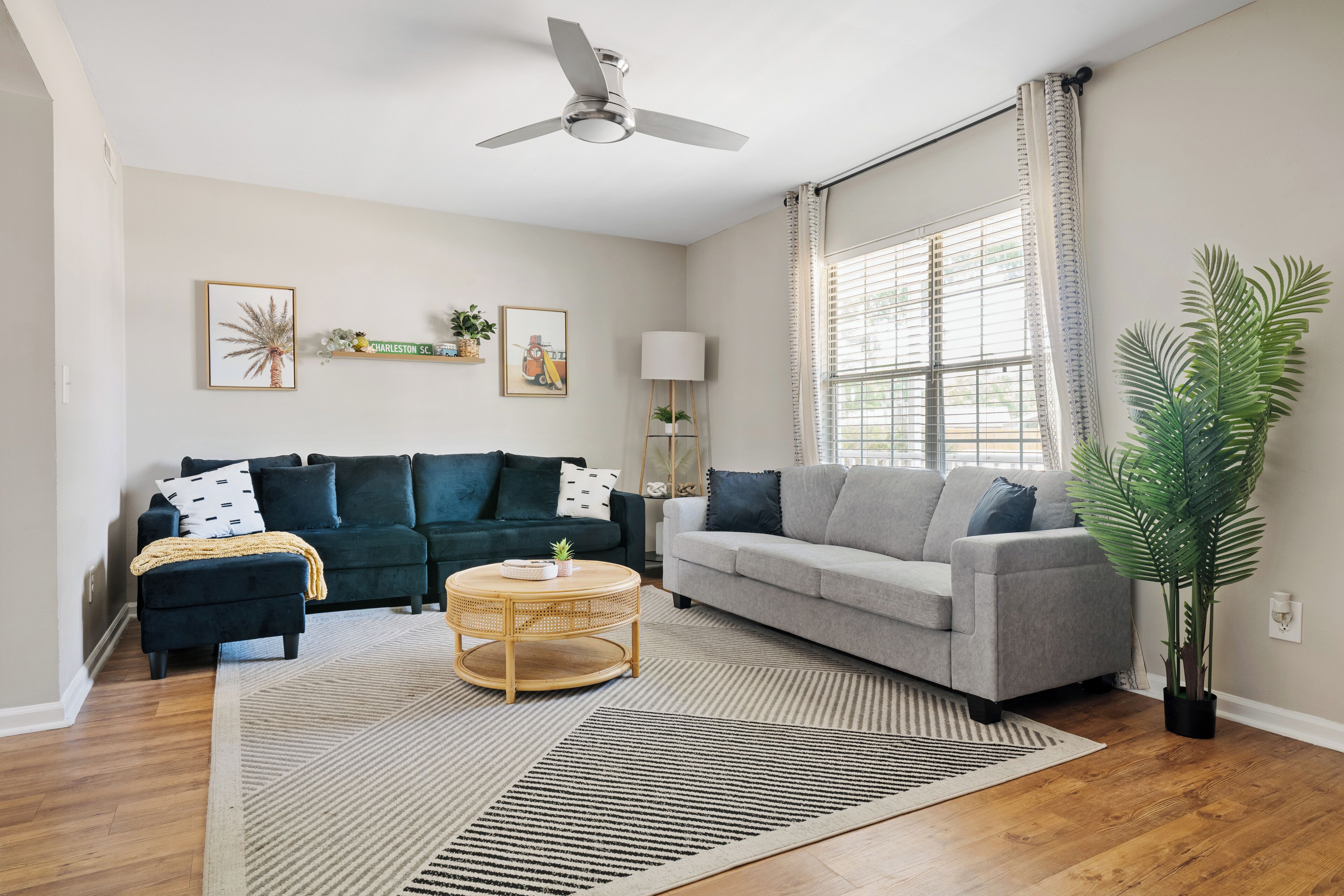 A living room with two sofas, a coffee table, a ceiling fan, and a large window with curtains.