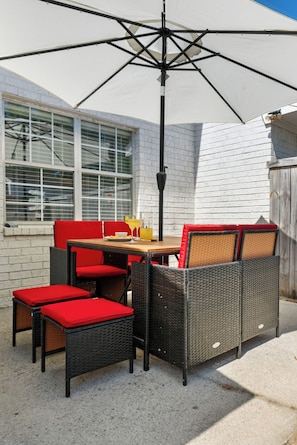 Un patio con mobiliario de mimbre, una mesa y una sombrilla grande.