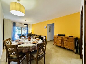 A dining area with a round table, chairs, a chandelier, a sofa, and a kitchen area with cabinets. - Caleta CostaBravaSi - Rest 650 m from the beach (Castell d'Aro)