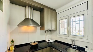 A modern kitchen with a stainless steel range hood, wooden cabinets, a black countertop, and a window with a view. - Caleta CostaBravaSi - Rest 650 m from the beach (Castell d'Aro)