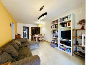 A living room with a sofa, dining table, chairs, a bookshelf, and a TV. - Caleta CostaBravaSi - Rest 650 m from the beach (Castell d'Aro)