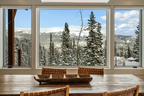 A dining area with a wooden table and chairs, large windows with a snowy mountain view. - *New* Moonlight Basin Ski-In/Out Luxury Townhome (Big Sky)
