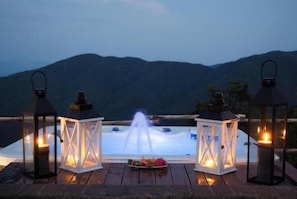 A hot tub with a waterfall feature, surrounded by lanterns and a plate of fruit.