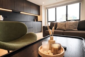 A modern living room with a green chair, a coffee table with decorative items, a sofa, and a city view through large windows. - Industrial Luxe 2BR Designer Flat near Victoria (Greater Manchester)