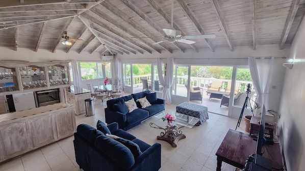 A spacious living area with a high ceiling, a bar area with glass display cases, and a seating arrangement with sofas and a coffee table. - Luxurious and spacious Caribbean Villa with large private pool (Gros Islet)